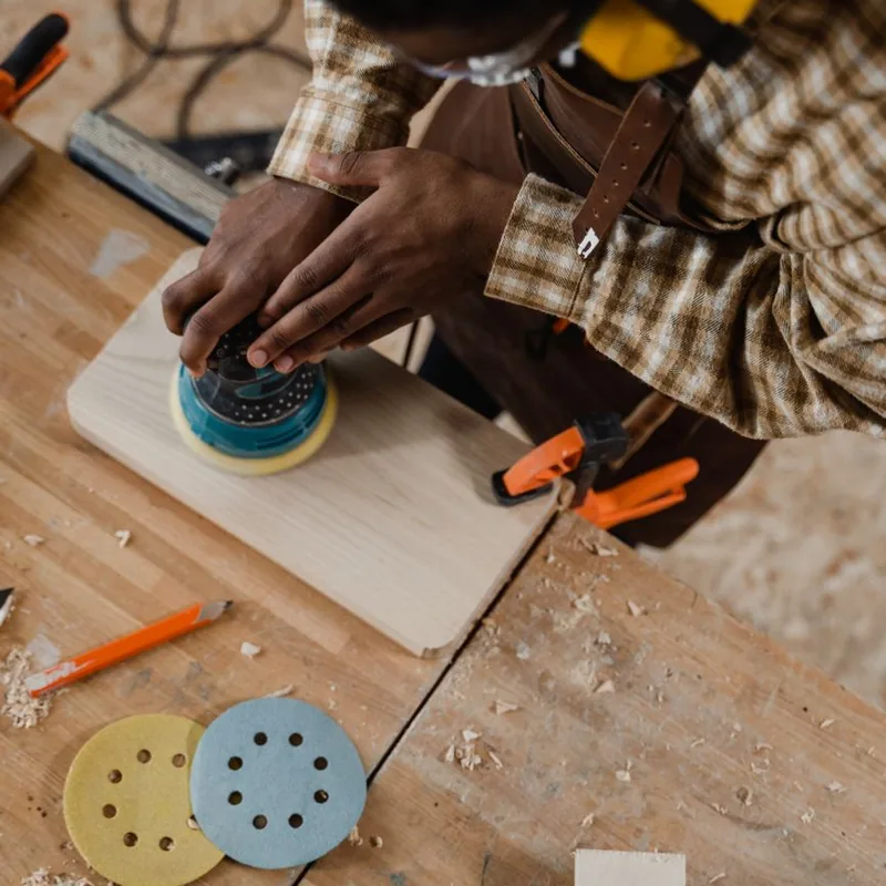 Joiner sanding a timber panel clamped to a workshop bench